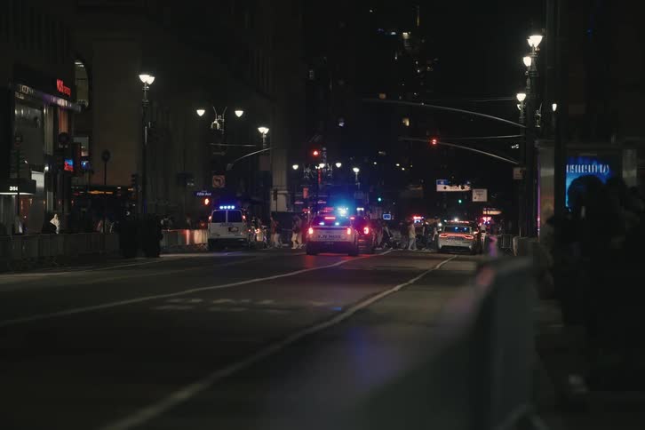 NYPD police cars with flashing blue lights create a blockade on a busy city street at night