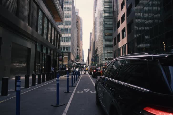 A point-of-view shot slowly advances down a busy urban street, flanked by towering modern skyscrapers and congested traffic