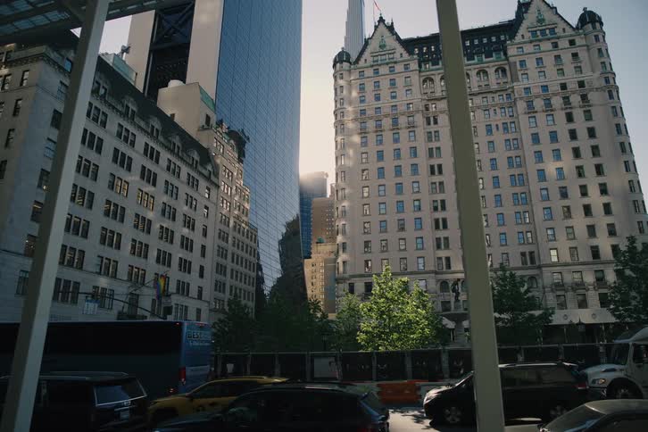 A slow reveal of a bustling New York City street corner with iconic buildings, heavy traffic, and a bright sun flare