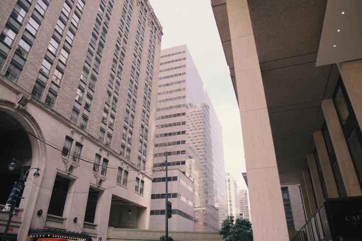 A slow push-in shot from underneath an overhang reveals a bustling city street surrounded by towering skyscrapers