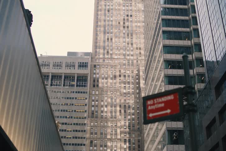 A slow tilt-up reveals the towering architecture of classic and modern skyscrapers on a city street
