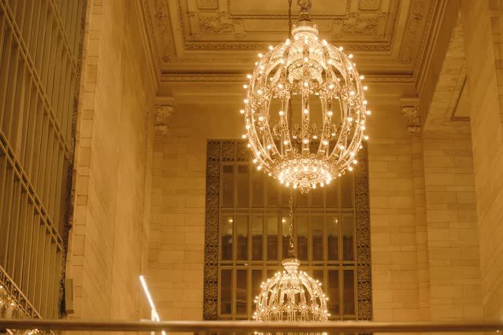A slow pan shot reveals the iconic and ornate chandeliers illuminating the interior of Grand Central Terminal in New York City