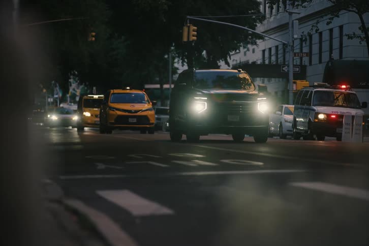A cyclist and a city bus move through a busy New York City intersection at dusk with traffic and police cars nearby
