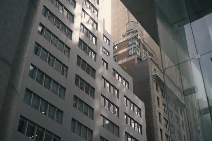 A slow dolly shot looking up through an urban canyon reveals a mix of modern and classic city architecture