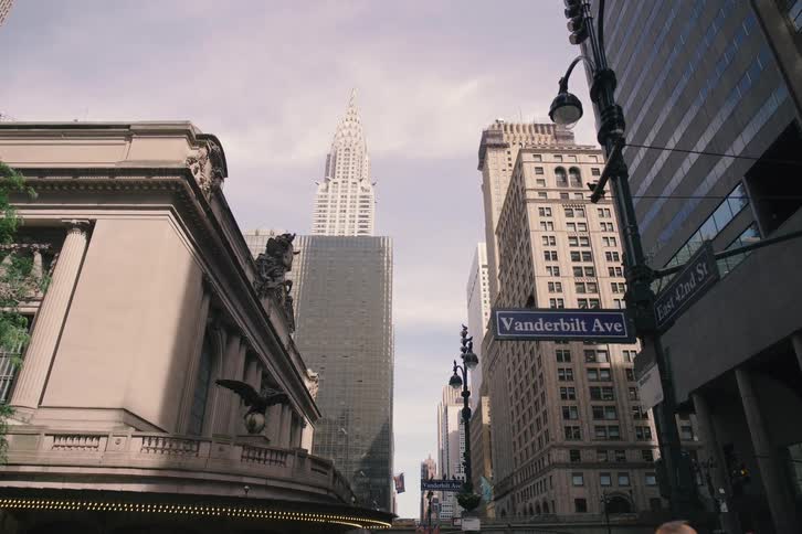 A slow-motion, low-angle push-in shot reveals the iconic Chrysler Building towering over Vanderbilt Avenue next to Grand Central Terminal in New York City