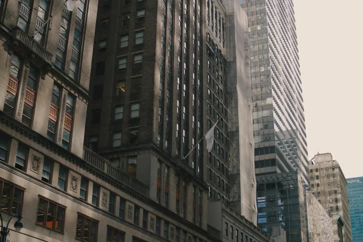 Low-angle shot of classic New York City architecture juxtaposed with modern skyscrapers as flags wave in the wind