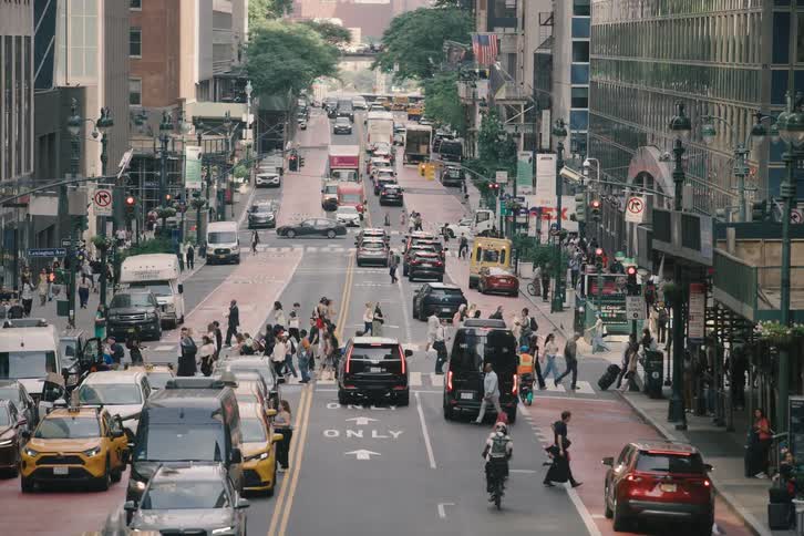 Busy city life unfolds from a high angle as pedestrians cross a bustling street filled with cars and yellow taxis in New York City