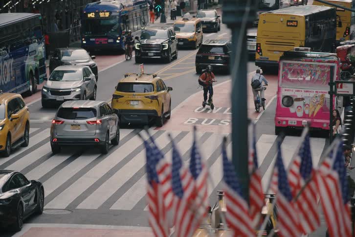 American flags overlook a busy New York City street as traffic moves in slow motion
