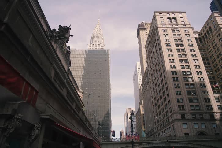 A cinematic slow-motion dolly shot pulls back from the Chrysler Building to reveal the iconic Grand Central Terminal on Vanderbilt Avenue in New York City