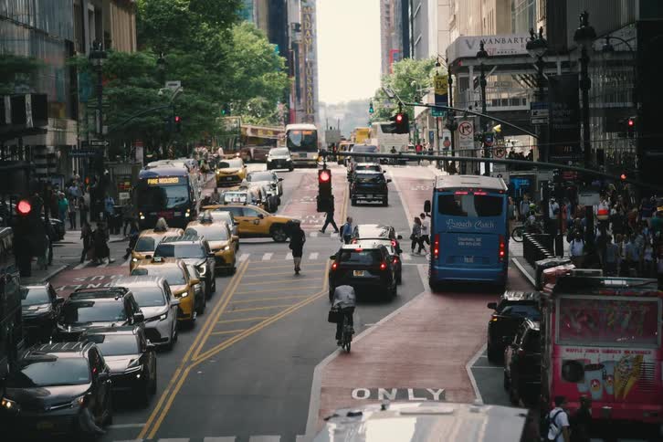 A high-angle static shot captures the bustling street life of New York City, with heavy traffic and pedestrians filling the frame