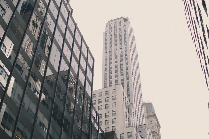 A slow pan reveals the impressive architecture of New York City skyscrapers, starting with the reflections in a modern glass facade on a cloudy day
