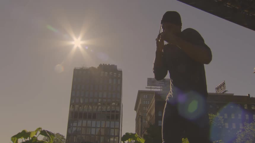 Slow motion shot of a man shadowboxing in an urban setting, silhouetted against a bright sun and city building