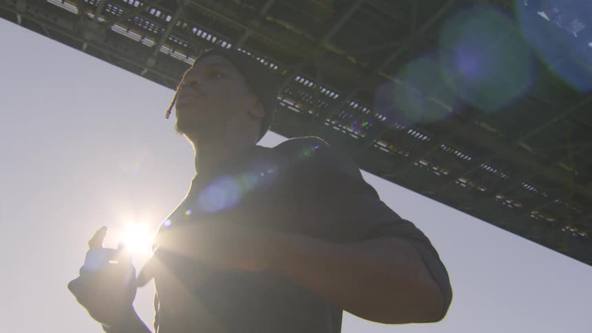 A determined man jogs in place under a large city bridge at sunset in a low angle, slow motion shot
