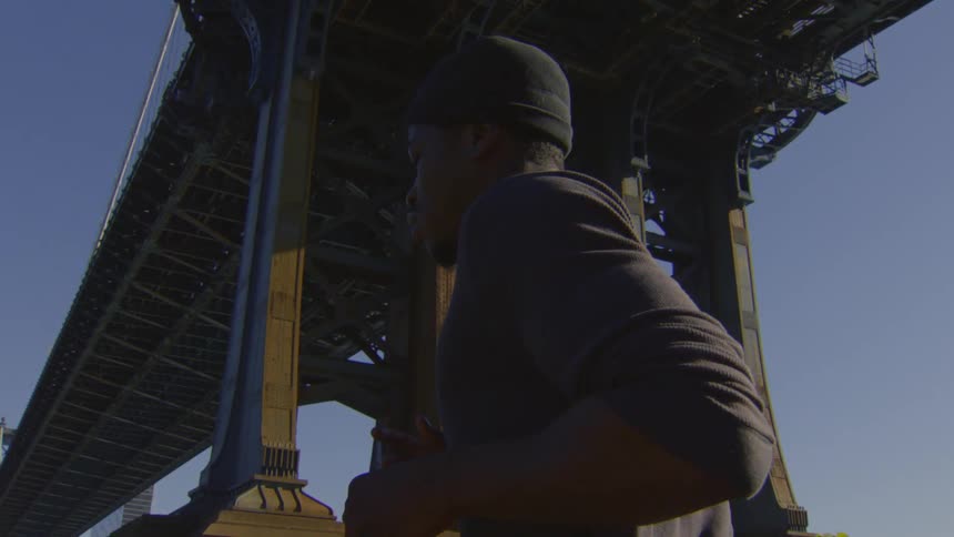 A fit man jogs in slow motion under the massive Manhattan Bridge on a sunny day