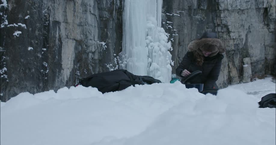 A woman cooks food in a pot in the snowy wilderness
