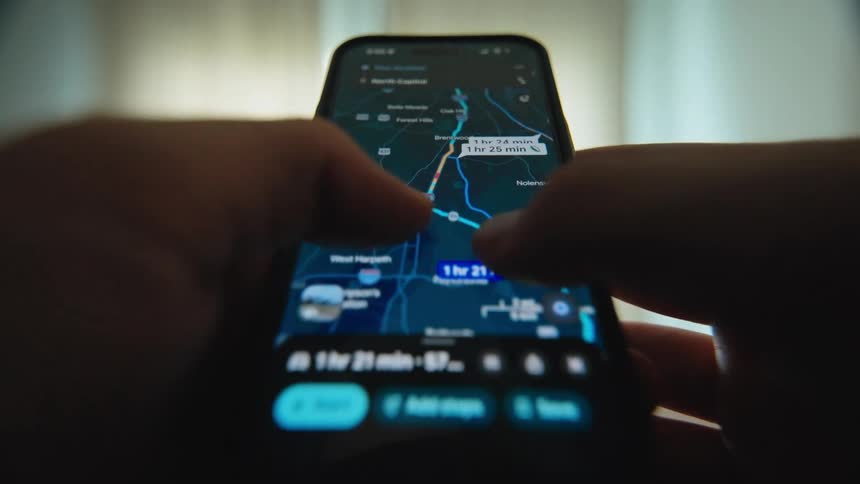 Close-up of a person using a navigation app on a smartphone to plan a driving route and check traffic