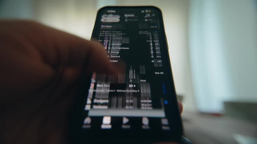 A close-up POV shot of a person scrolling through a sports news feed and live scores on a smartphone app