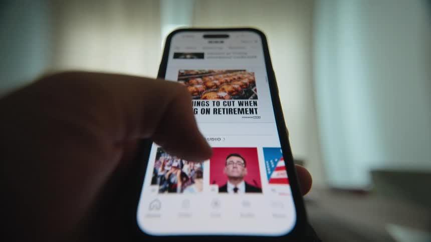 Close-up of a person's thumb scrolling through a news feed on a smartphone to stay updated on current events