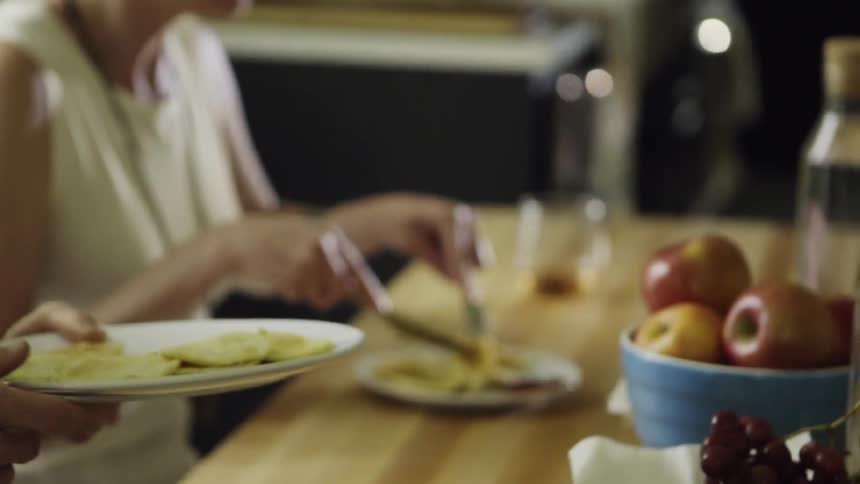 A dinner guest is cutting her food while another guest passes a plate