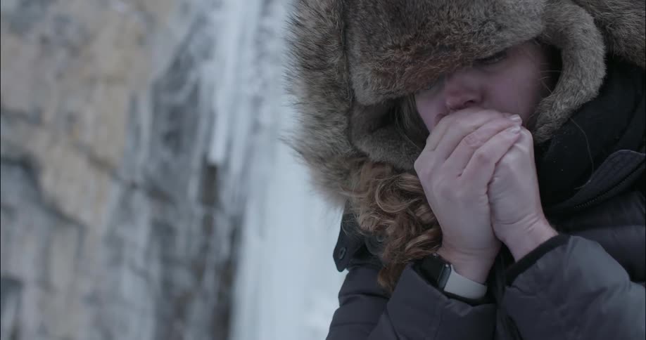 A woman rubs her hands together and blows on them to get warm