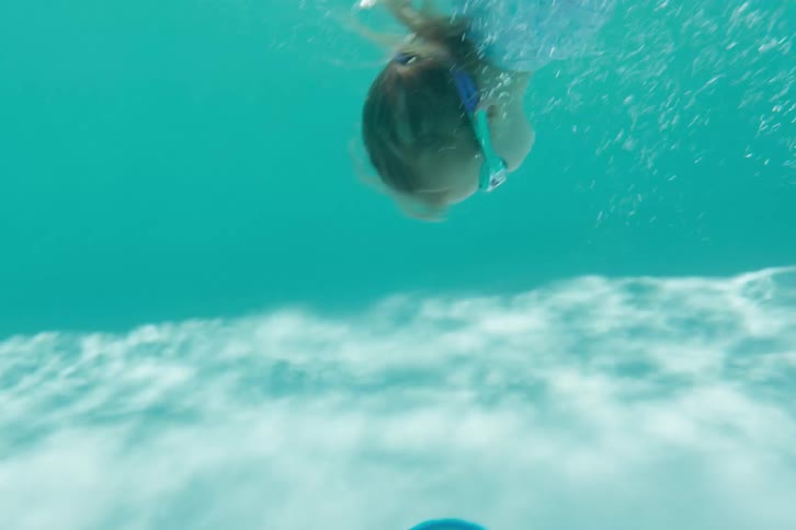 Slow motion shot of a young girl with goggles jumping into a swimming pool, then going underwater to retrieve toys from the bottom