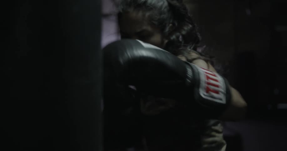 A woman hits a punching bag while wearing boxing gloves