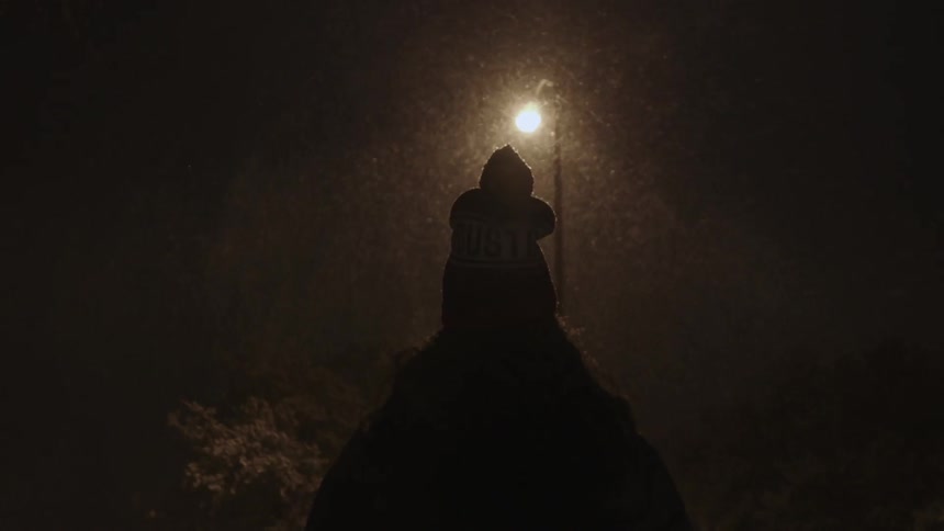 A person in a hat stands outside in the snow at night