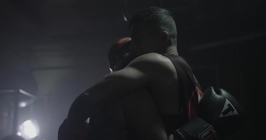 Man wearing boxing gloves hugs a woman in a dimly lit gym