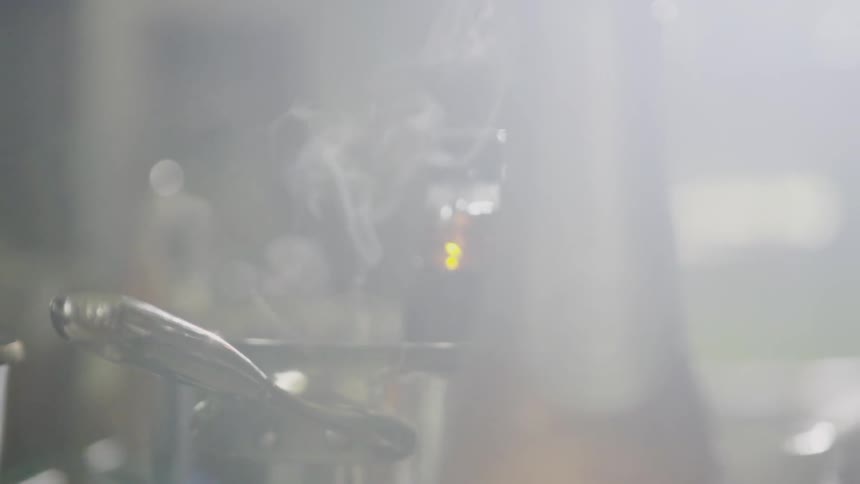 Steam rises from a saucepan set on a stovetop with a bottle of syrup in it