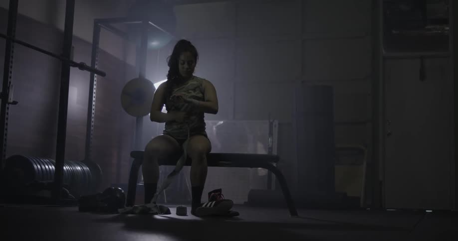 Woman wrapping her hand with hand wrap in dark gym