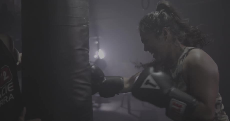 A woman rests then punches a heavy bag repeatedly