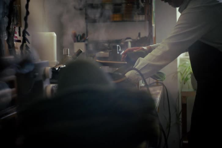 Artisan hat maker meticulously steams the brim of a classic fedora in a dimly lit workshop