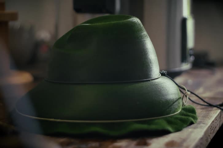 A close-up shot of a traditional green felt hunting hat resting on a wooden surface
