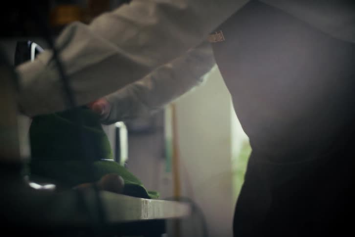 A skilled milliner in a workshop meticulously shapes and crafts a green felt hat using traditional tools
