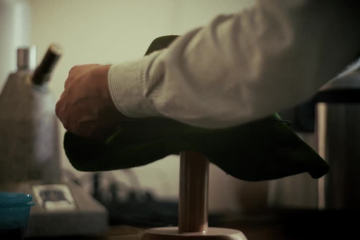 A skilled artisan meticulously ties a cord and shapes a traditional green felt hat on a wooden form in a vintage workshop