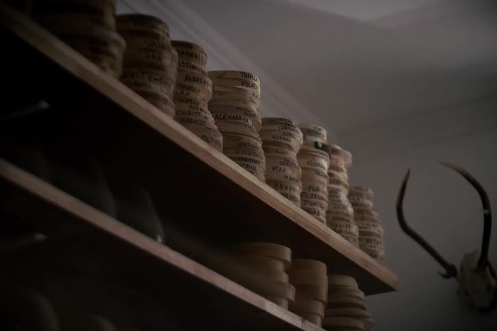 Low angle static shot of custom wooden head molds with client names on shelves in a traditional hat maker's workshop