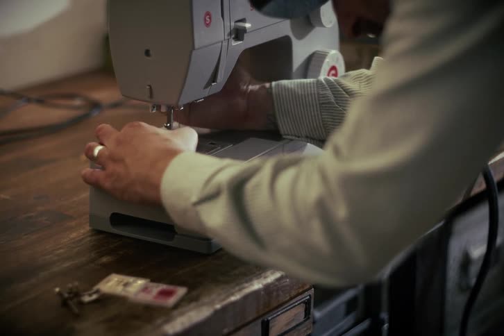 A close-up shot of a craftsman's hands carefully setting up a modern Singer sewing machine on a wooden workbench