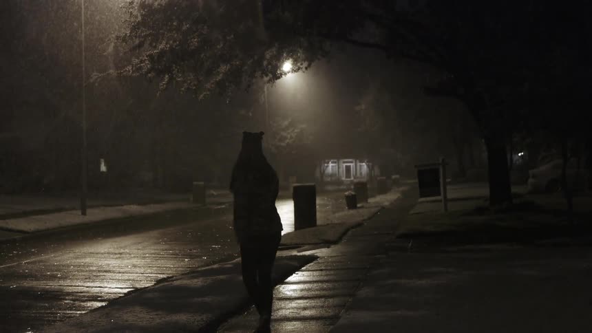 A woman spins while walking down the sidewalk at night