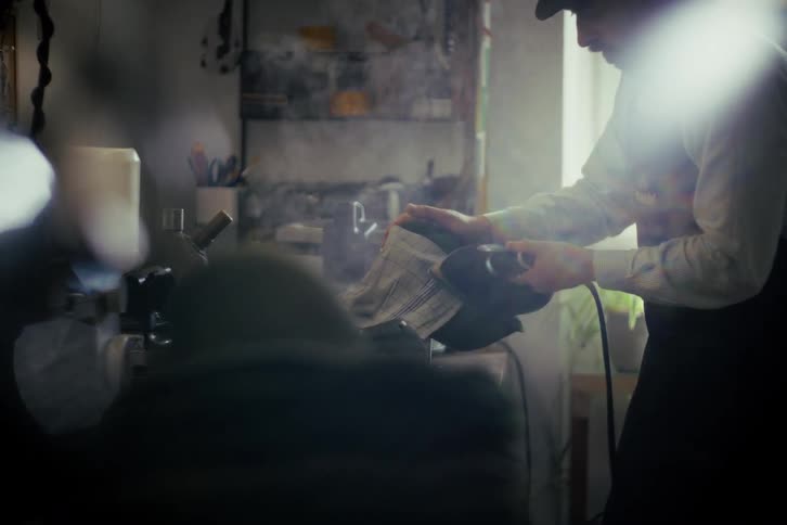 A hatter meticulously steams and shapes a felt hat brim in his sunlit workshop