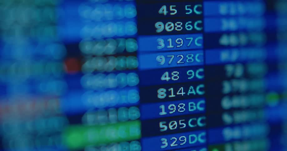 A close-up, shallow focus shot of a digital stock market ticker shows prices and data rapidly changing on screen