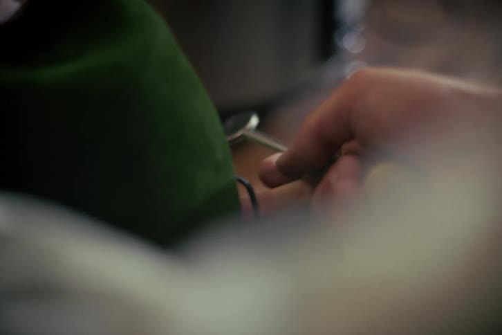 A master upholsterer carefully presses the seams of a plush green velvet fabric with a specialized burnishing tool