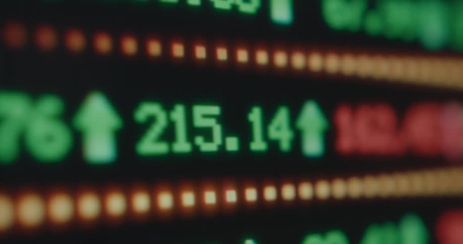Rapidly fluctuating stock market numbers and symbols are displayed on a digital ticker screen