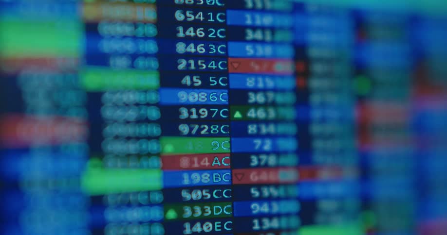 A blurry close-up of a digital stock market ticker shows financial data changing rapidly on a blue screen