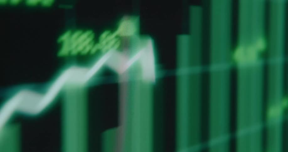 A blurry, abstract close-up of a green stock market chart on a digital screen, with graphs and data showing upward trends and growth
