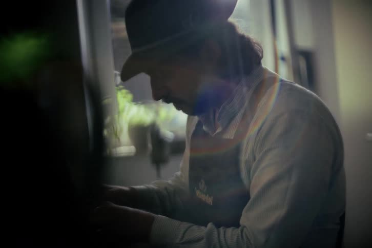 Dreamy, nostalgic shot of a traditional craftsman in a hat and apron working diligently in his sunlit workshop