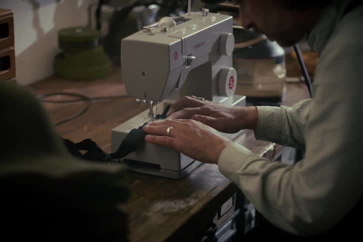 A man carefully sews a piece of black fabric on a modern Singer sewing machine in a workshop