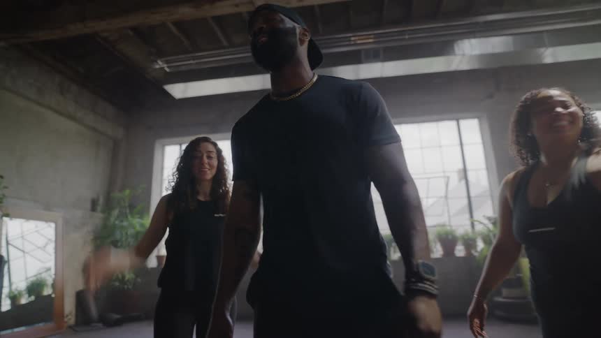 An energetic fitness instructor leads a smiling and diverse class in a sunlit urban loft gym