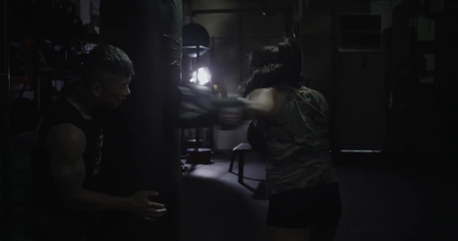 Woman boxer hitting a heavy bad being held in place by a trainer
