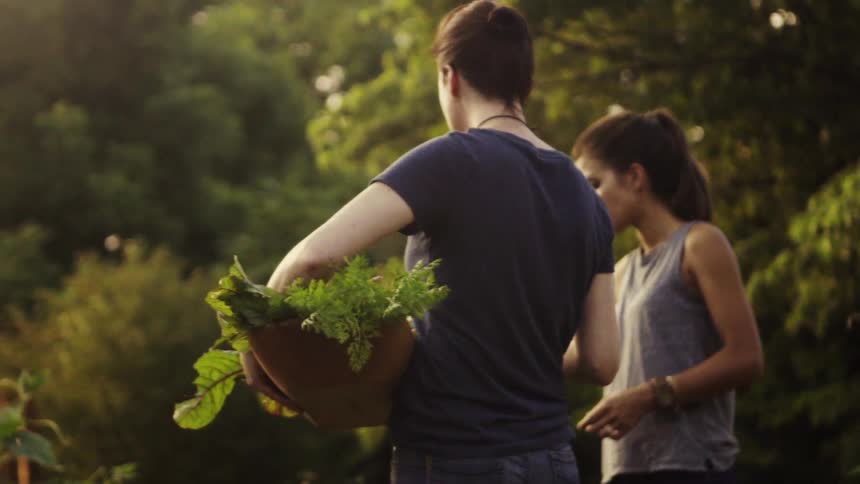 Woman carrying a basket with greens and another woman eats something