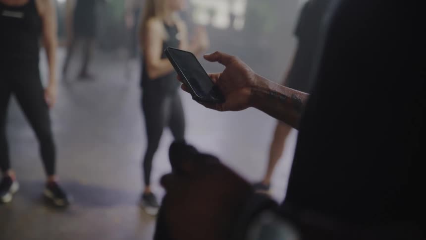 Over-the-shoulder close-up of a personal trainer using a smartphone to manage a group fitness class